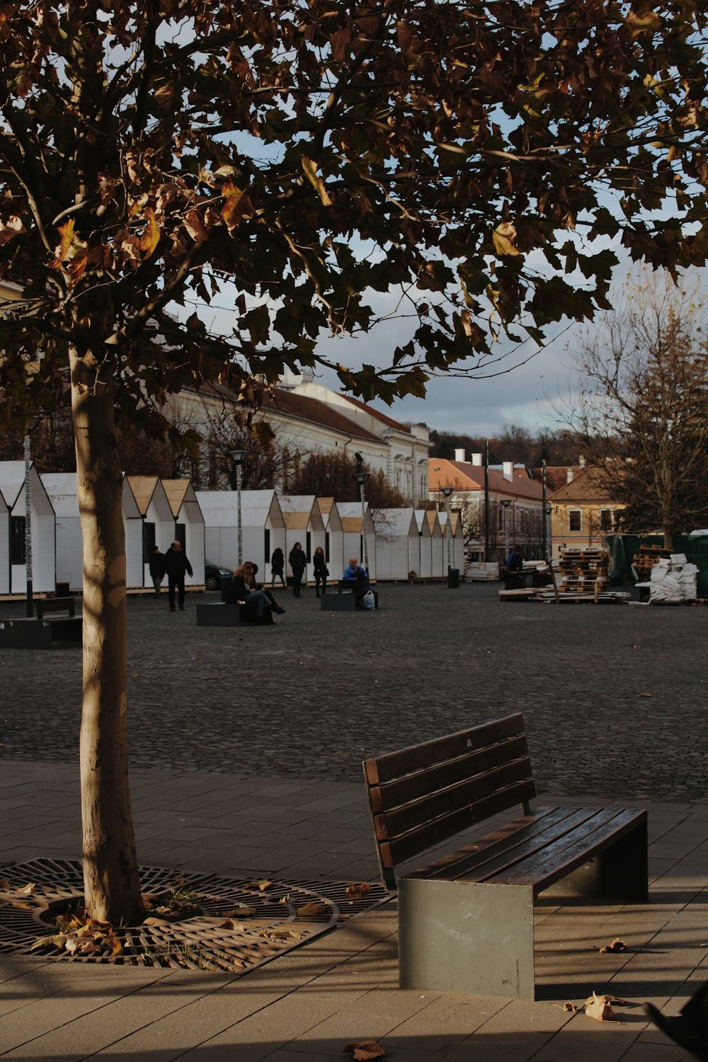 people walking on sidewalk near brown wooden bench during daytime