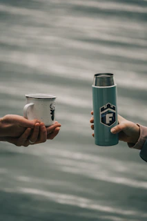 A 316 stainless steel thermal mug with condensation beads, held by a hand outdoors.