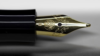 A close-up view of a fountain pen nib, highlighting intricate engravings and a glossy black pen barrel. The nib displays delicate scrollwork and a circular emblem.