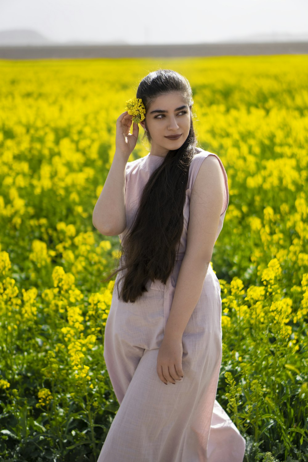 woman in white tank top standing on yellow flower field during daytime