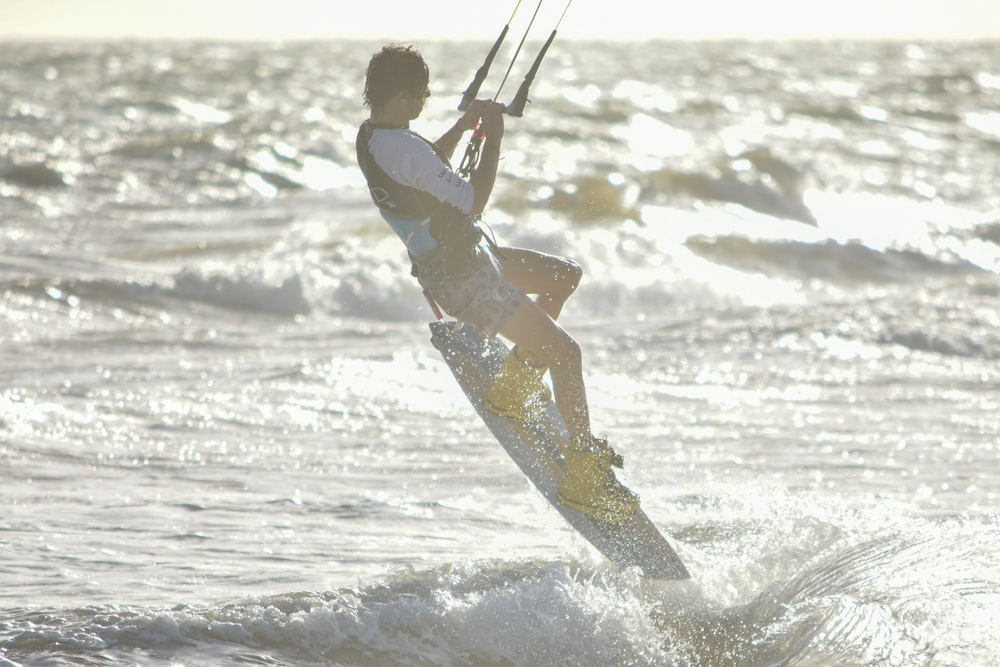 Mann in weißem Hemd und braunen Shorts fährt tagsüber auf weißem Surfbrett am Strand