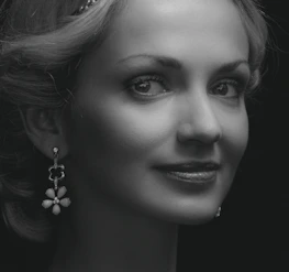 Lifestyle shot of a woman wearing classy earrings, smiling gently against a charcoal backdrop.