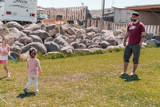 A father playing catch with his two young sons in a sunny backyard.