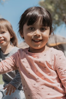 Smiling children wearing bright clothes playing outdoors on a sunny day.