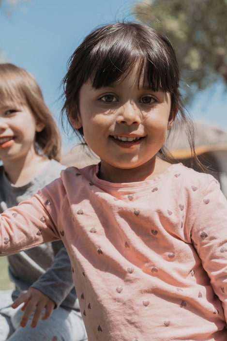 Two children, a boy and a girl, smiling and playing outdoors wearing bright and cheerful clothes.