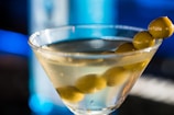 An elegant Martini glass filled with a clear drink, garnished with two green olives on a skewer