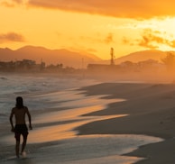 woman in black shirt walking on beach during sunset