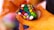 Hands are holding a colorful dodecahedron puzzle with various colored squares on each face. The background is softly blurred, emphasizing the puzzle. The person appears to be in the process of manipulating or solving the puzzle.