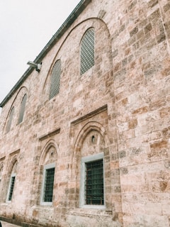 A historic stone building characterized by arched windows and intricate stonework. The structure features a series of evenly spaced windows with protective grilles, and the stone surface has a warm, textured appearance suggesting age and antiquity.