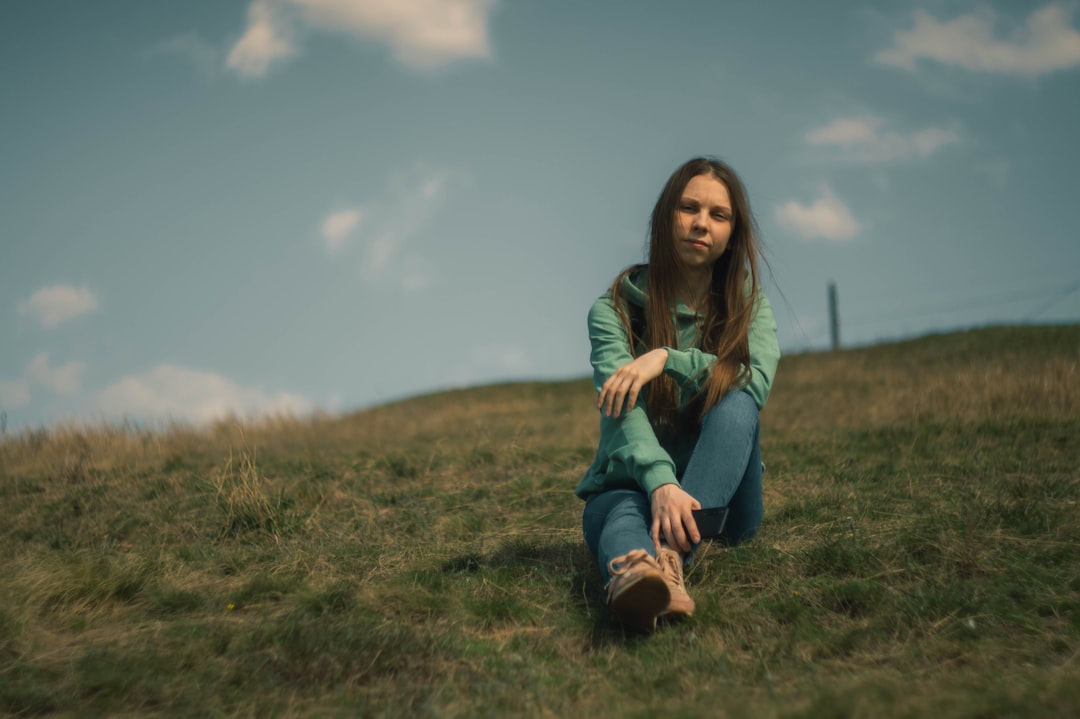 woman in green long sleeve shirt and blue denim jeans sitting on green grass field during