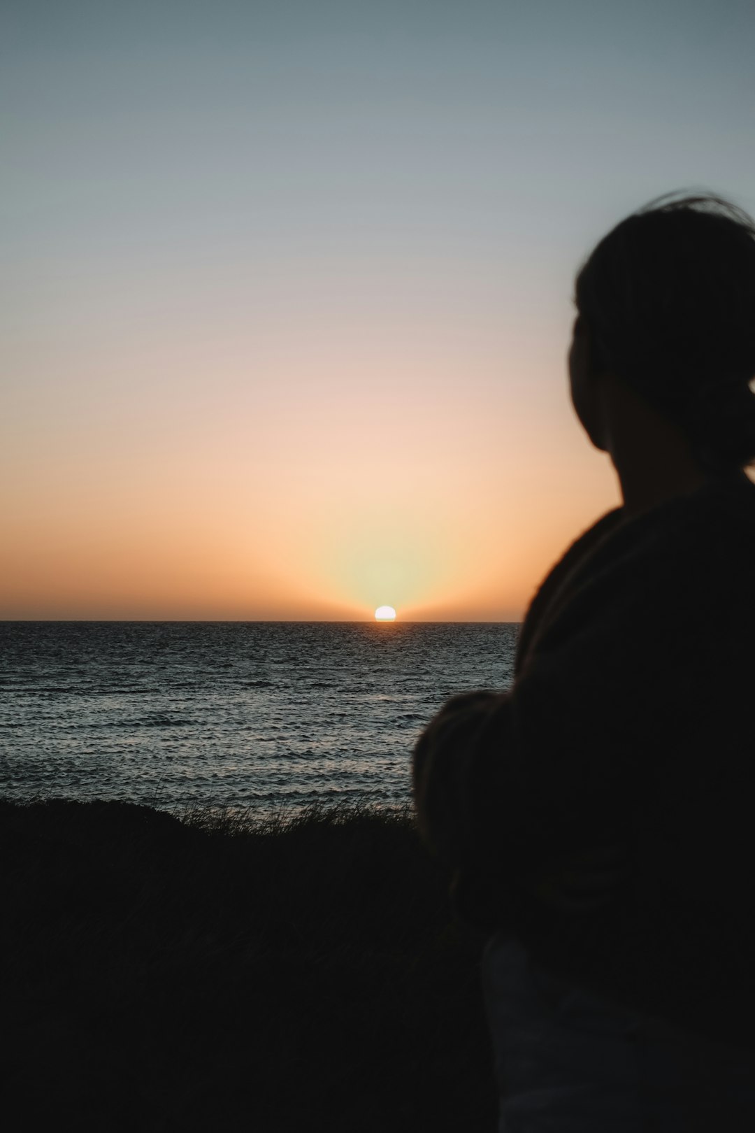 silhouette of man standing near body of water during sunset