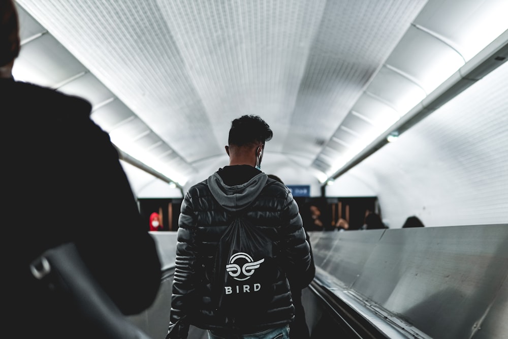 man in black and white adidas jacket standing on escalator