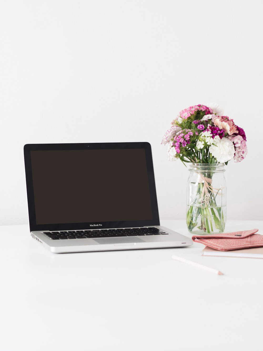 MacBook Pro junto a flores rosas y blancas en un jarrón de vidrio transparente