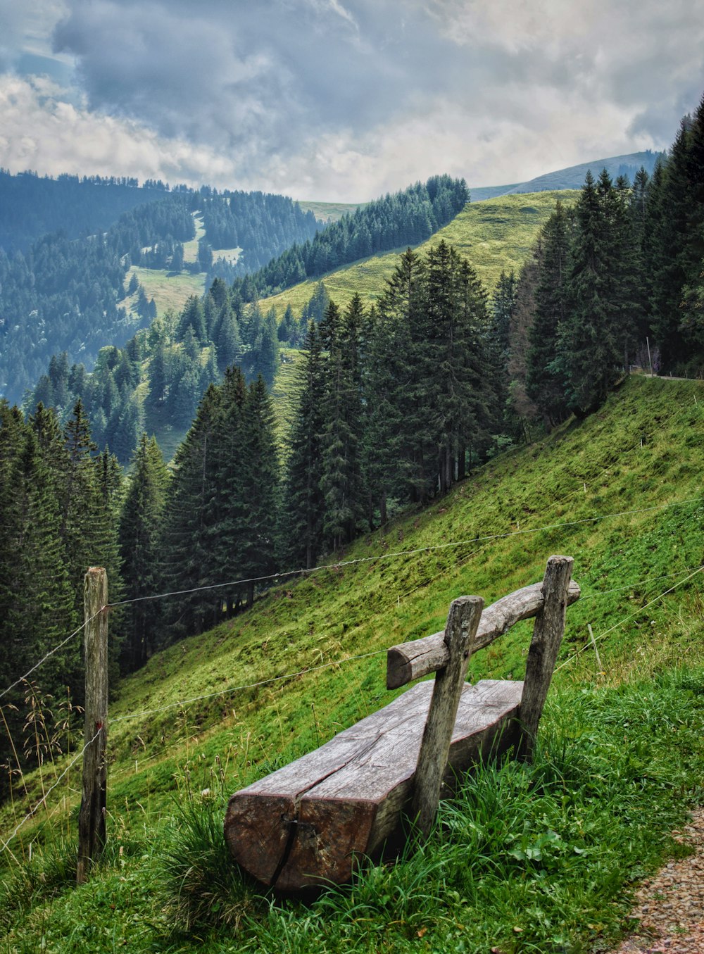 valla de madera marrón en un campo de hierba verde cerca de árboles verdes y montañas durante el día