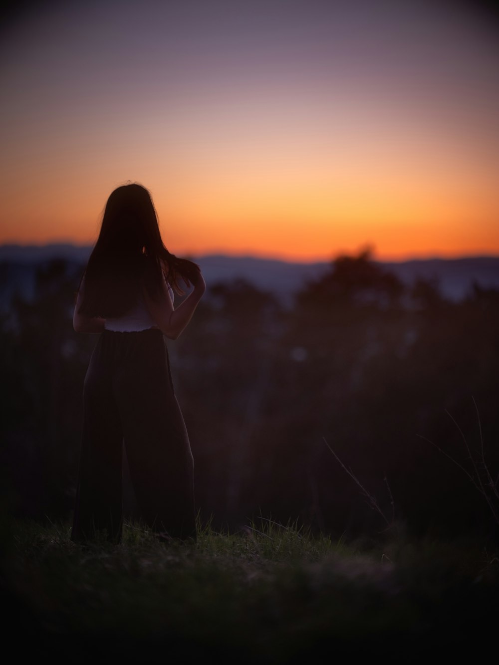 Silueta de mujer de pie en el campo de hierba durante la puesta del sol