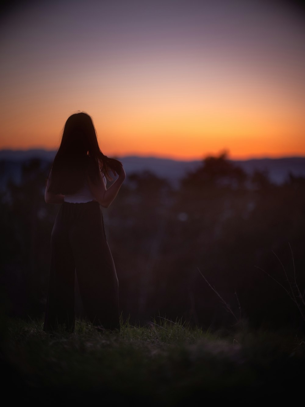 silhouette of woman standing on grass field during sunset