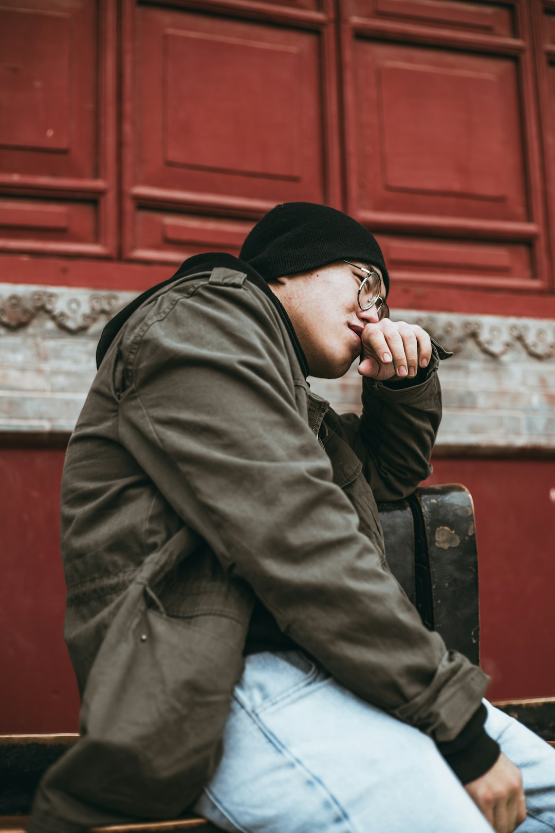 man in black hoodie and blue denim jeans sitting on red wooden bench