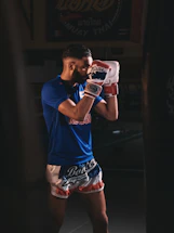 A focused Muay Thai coach demonstrating a precise strike in a sunlit gym.