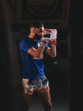A focused Muay Thai coach demonstrating a precise strike in a sunlit gym.