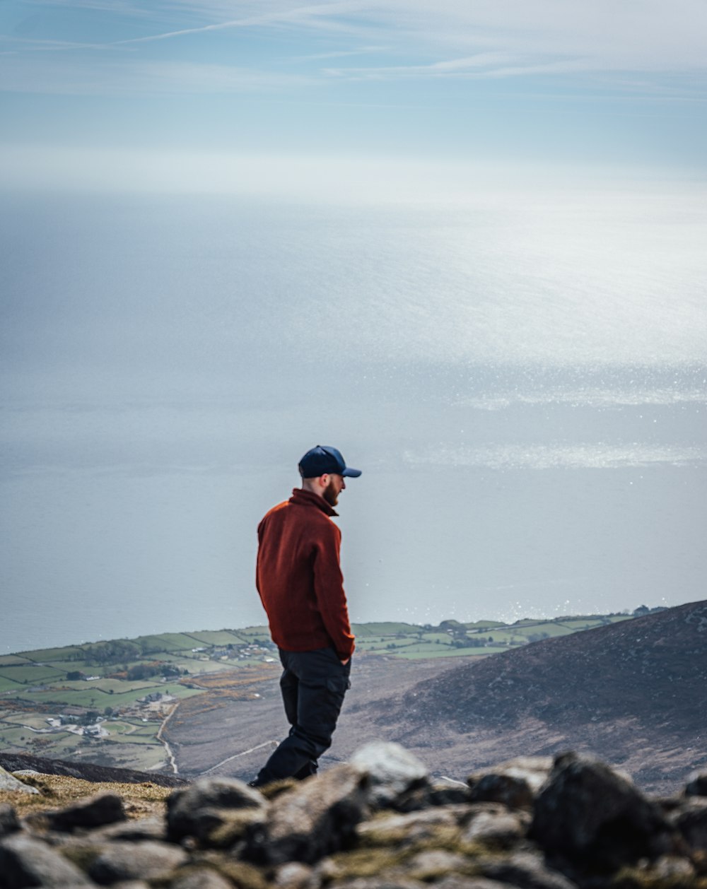 uomo in giacca rossa in piedi sulla formazione rocciosa vicino allo specchio d'acqua durante il giorno