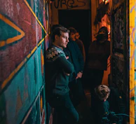 Dynamic group shot of the label’s artists standing against a charcoal gray wall accented by neon purple graffiti.