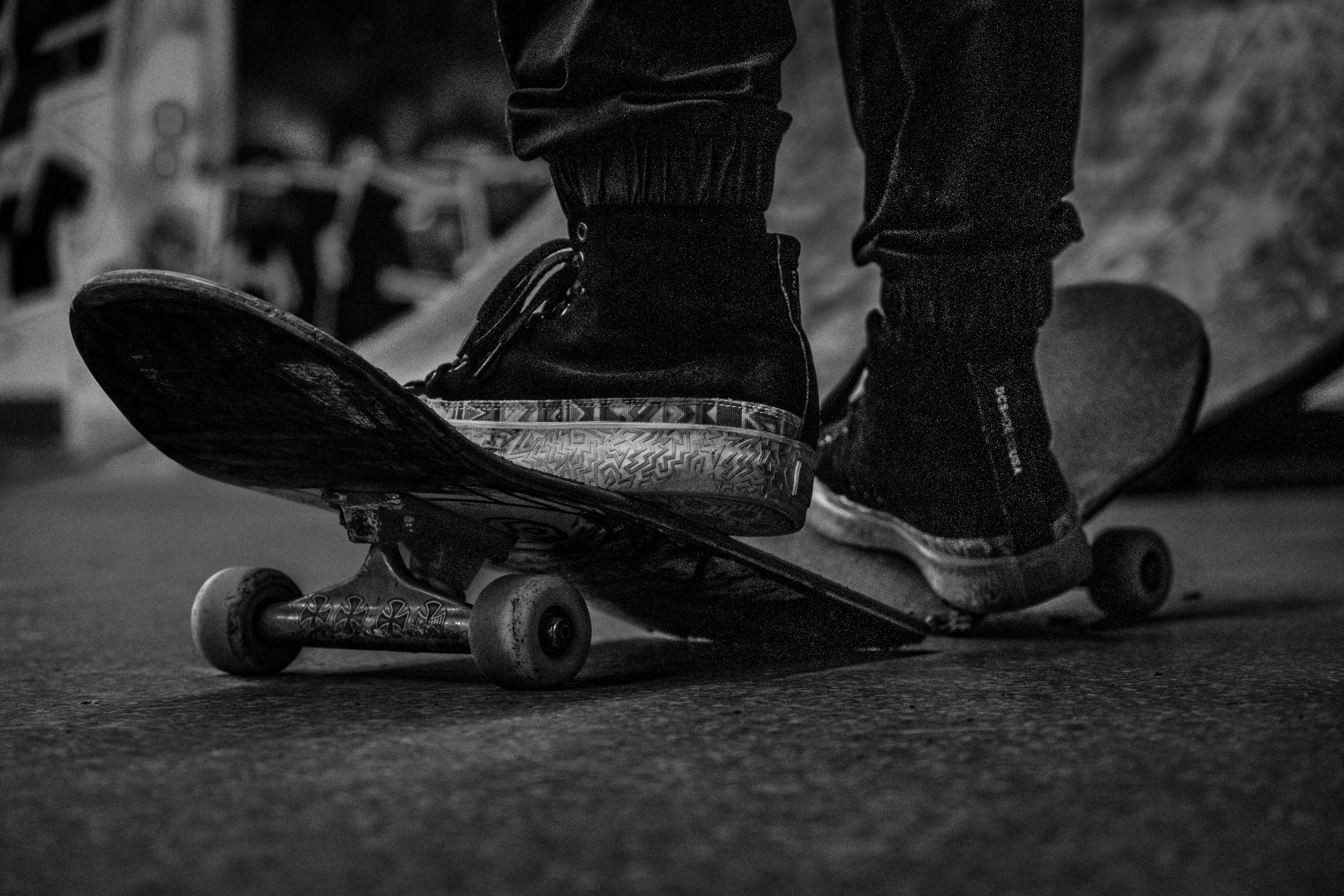 grayscale photo of person wearing black boots and black denim jeans riding skateboard
