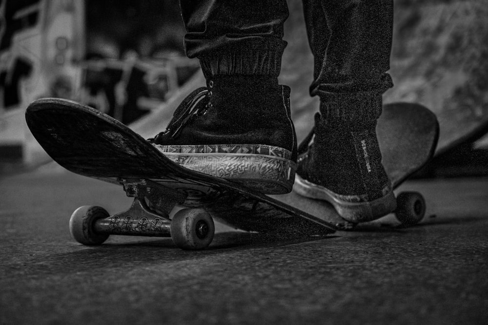 Photo en niveaux de gris d’une personne portant des bottes noires et un jean en denim noir faisant du skateboard