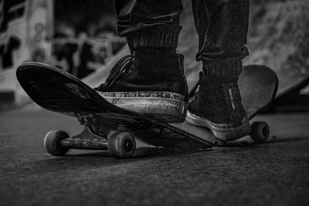 grayscale photo of person wearing black boots and black denim jeans riding skateboard