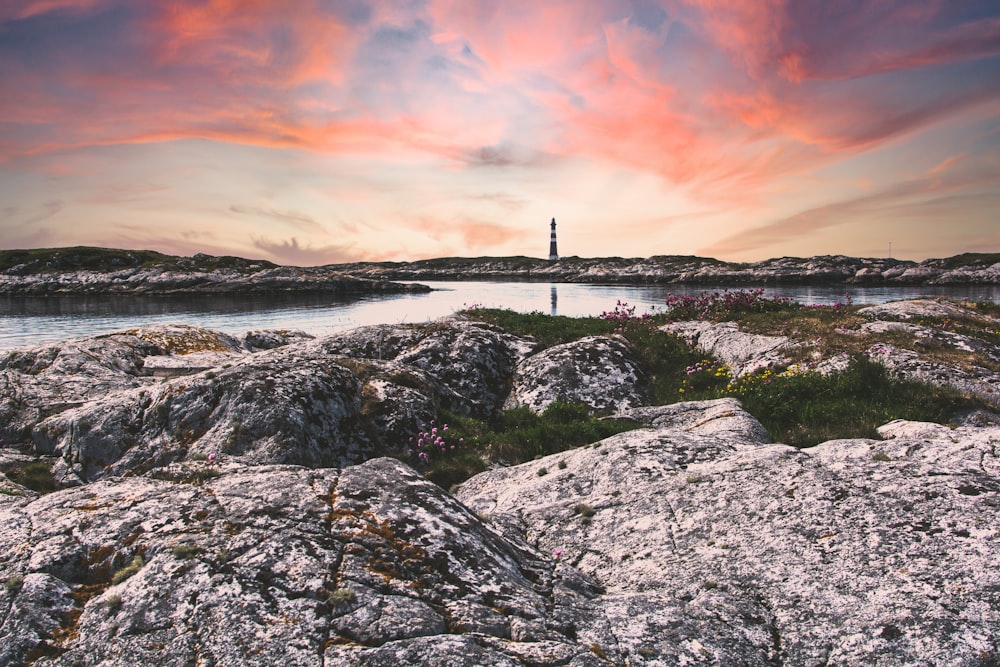 black and white lighthouse on gray rocky shore during sunset