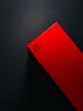 A red rectangular box with sharp angles is positioned against a dark background. The box features a logo with a distinctive symbol and the text '1+' on its surface.