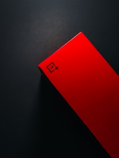 A red rectangular box with sharp angles is positioned against a dark background. The box features a logo with a distinctive symbol and the text '1+' on its surface.