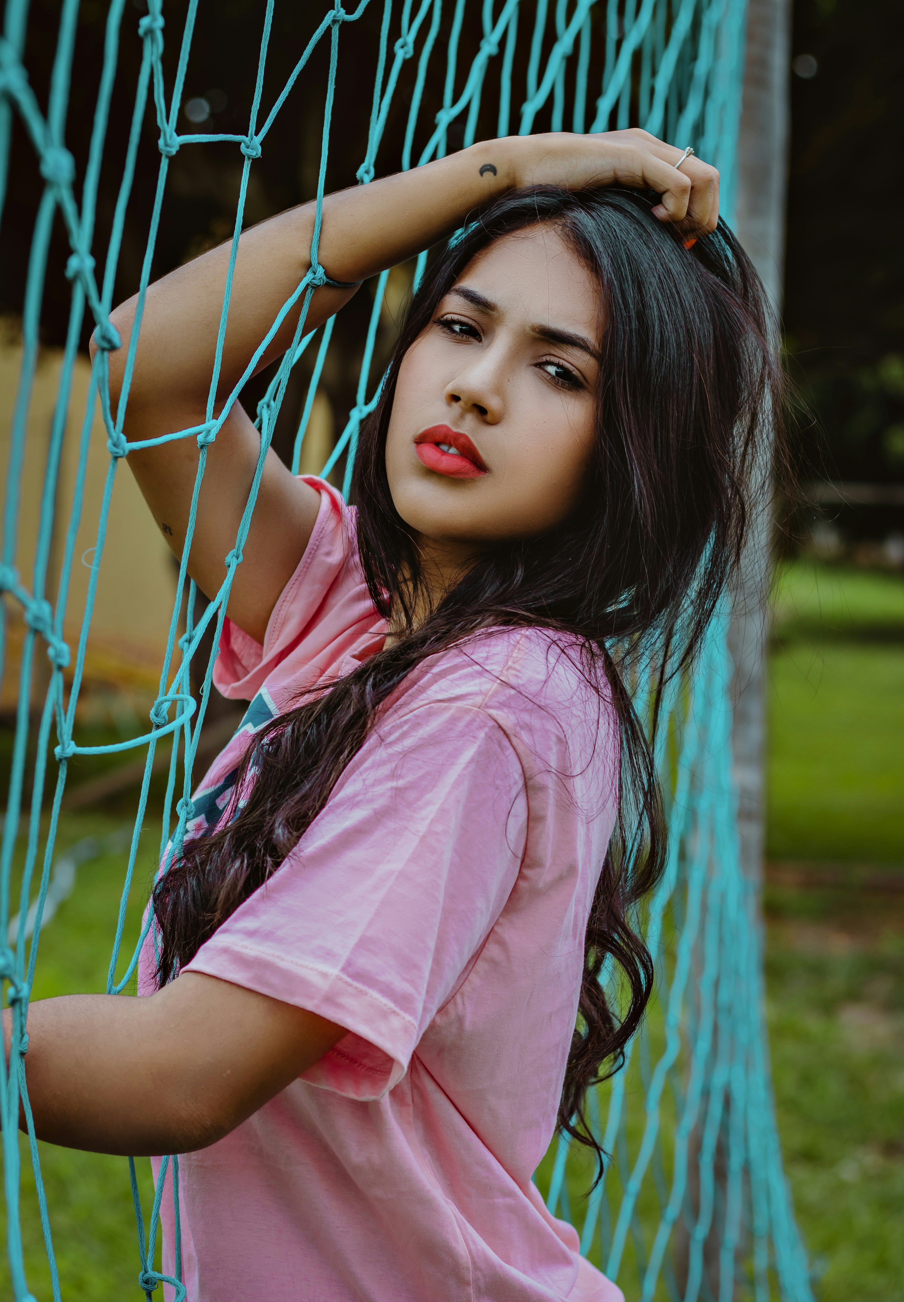 Gadis dengan kaos merah muda berdiri di lapangan rumput hijau di siang hari