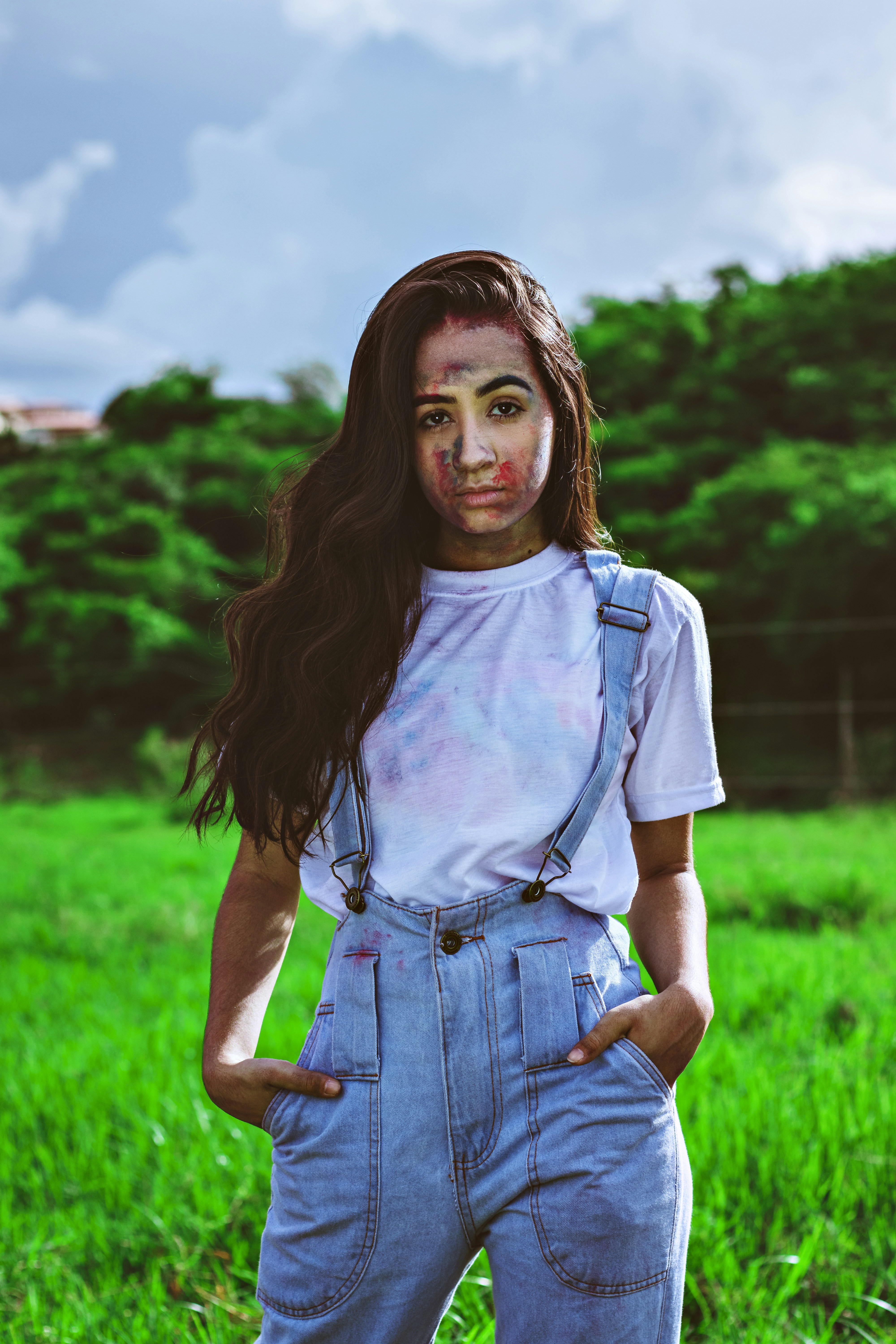 Wanita dengan tank top putih dan dungaree denim biru berdiri di lapangan rumput hijau di siang hari