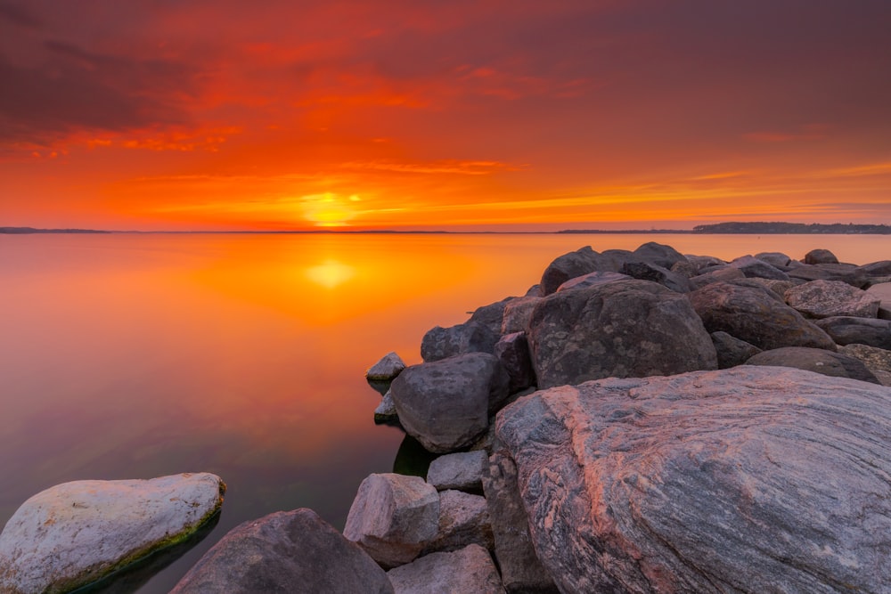 gray and brown rocks beside body of water during sunset