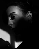 A dramatic black and white portrait of a person with strong shadows and highlights accentuating their features. The lighting creates a moody and introspective feel, with the focus on the person's profile.