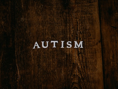 The word 'AUTISM' is centered on a rustic, dark wooden background. The texture of the wood is rough and weathered, adding a natural and organic feel to the image.