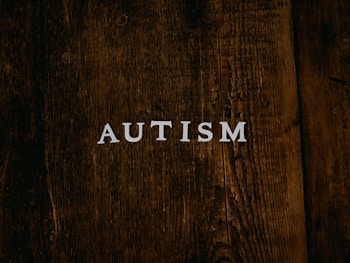 The word 'AUTISM' is centered on a rustic, dark wooden background. The texture of the wood is rough and weathered, adding a natural and organic feel to the image.