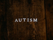 The word 'AUTISM' is centered on a rustic, dark wooden background. The texture of the wood is rough and weathered, adding a natural and organic feel to the image.
