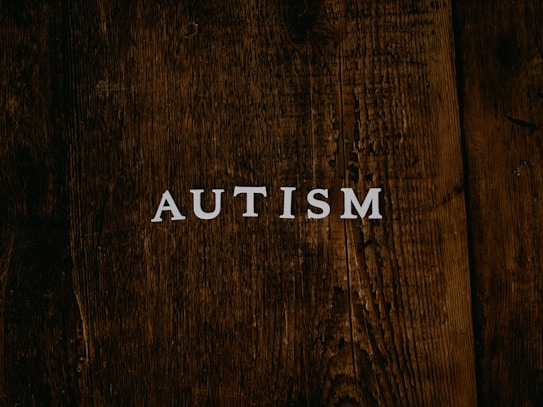The word 'AUTISM' is centered on a rustic, dark wooden background. The texture of the wood is rough and weathered, adding a natural and organic feel to the image.