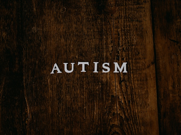 The word 'AUTISM' is centered on a rustic, dark wooden background. The texture of the wood is rough and weathered, adding a natural and organic feel to the image.