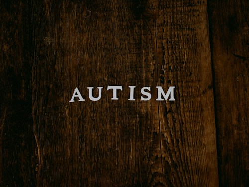 The word 'AUTISM' is centered on a rustic, dark wooden background. The texture of the wood is rough and weathered, adding a natural and organic feel to the image.