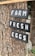 Wooden signs with the words 'FARM FRESH EGGS' are hanging on a tree. The signs are painted in black with white lettering and are attached with red twine. The background includes the bark of the tree and some greenery.