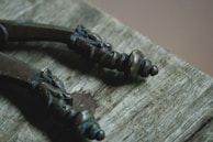 Close-up view of two intricately designed bronze handles with ornate detailing, lying on a weathered wooden surface.
