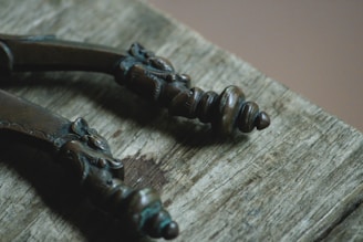 Close-up view of two intricately designed bronze handles with ornate detailing, lying on a weathered wooden surface.