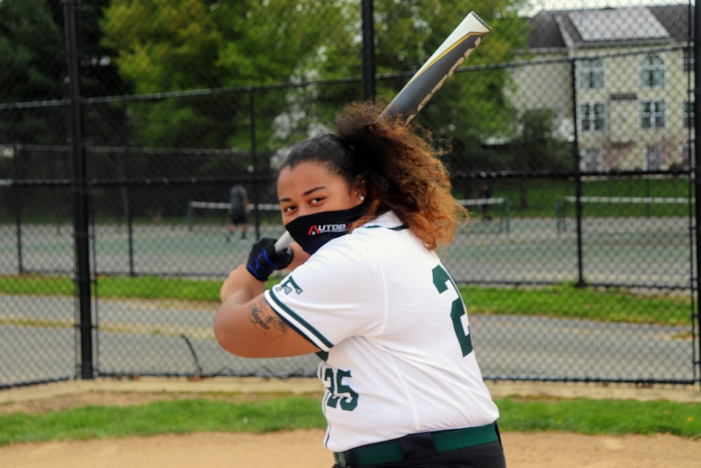 woman in white and blue jersey shirt holding baseball bat during daytime