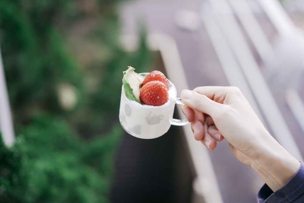 person holding white ceramic mug with strawberry and cream