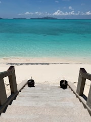 Sunlit sandy beach with crystal clear water just steps from a Mediterranean villa terrace.