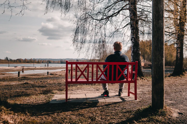 Woman sitting on a red bench by the water