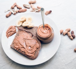 A close-up shot of creamy peanut butter being spread on fresh bread with peanuts scattered around.