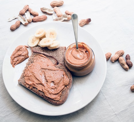 A close-up shot of creamy peanut butter being spread on fresh bread with peanuts scattered around.